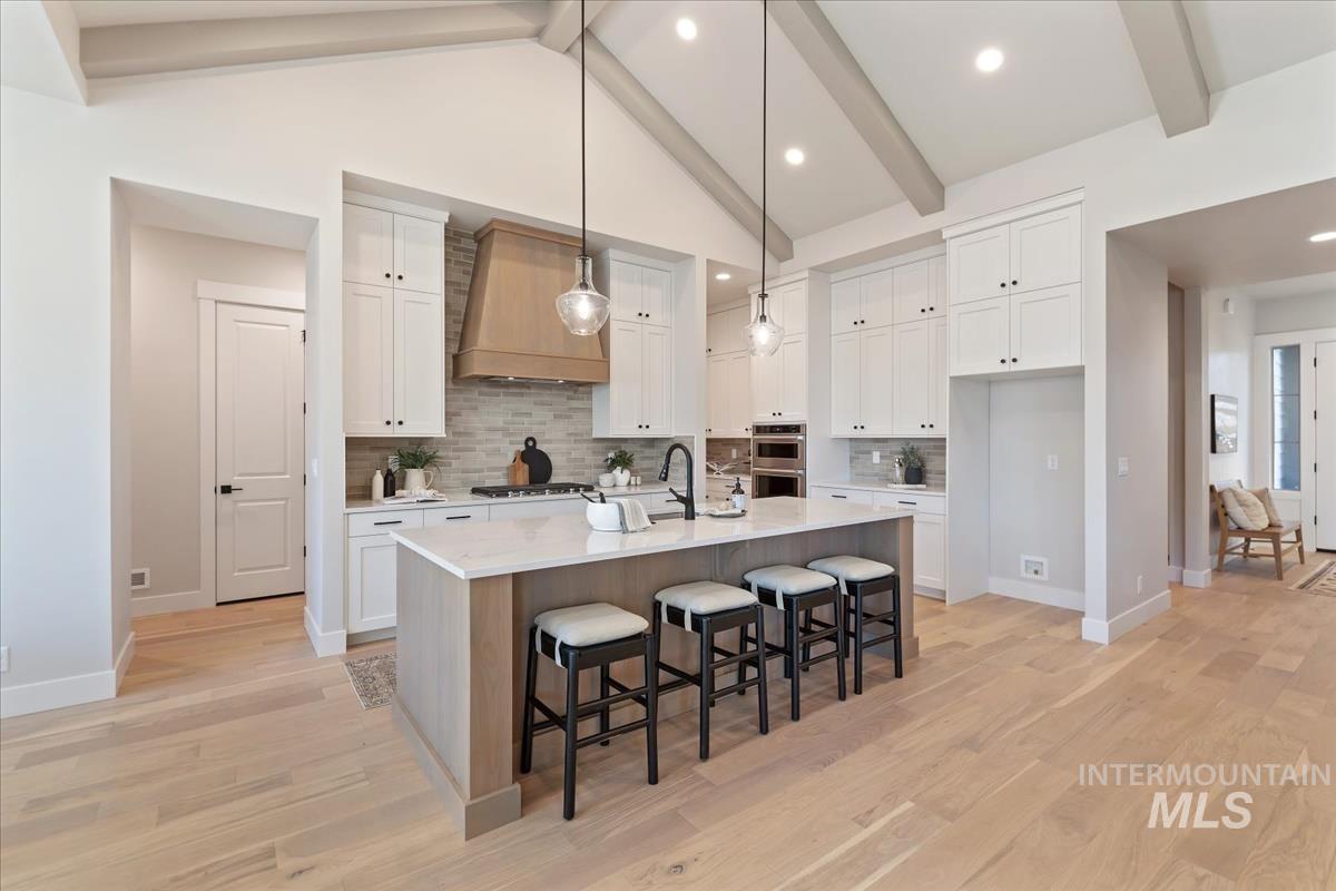 7355 Powell Place Eagle, ID 83714 - Photo 8 of 37 Kitchen featuring a large central island with seating, white shaker cabinetry, a light wood-finish range hood, integrated double ovens, and vaulted ceilings with exposed beams