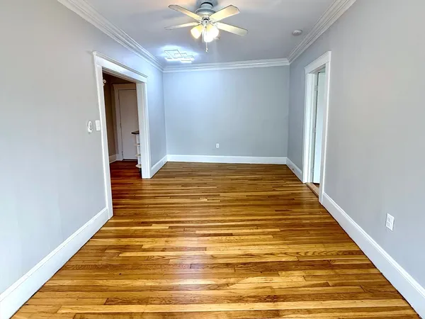 a view of an empty room with wooden floor and a chandelier fan