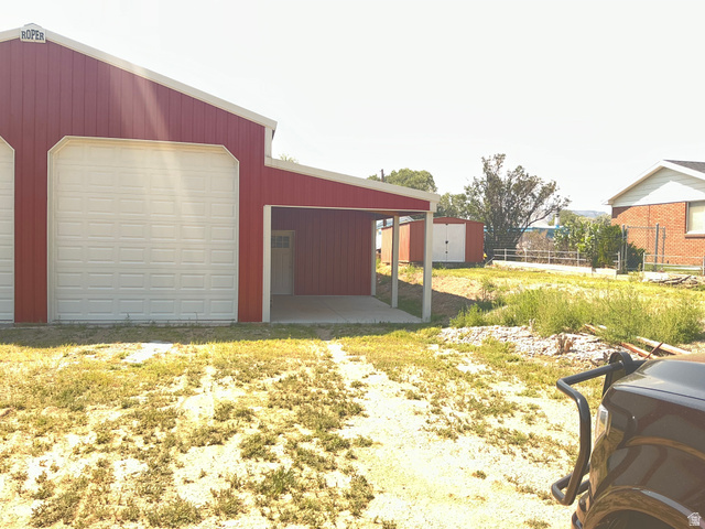 98 Main Street Manila, UT 84046 - Photo 29 of 36 Red metal-sided structure featuring multiple large roll-up doors, a covered concrete pad, and an entry door