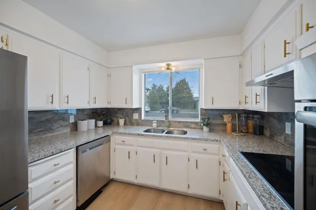 a kitchen with granite countertop white cabinets sink and stainless steel appliances
