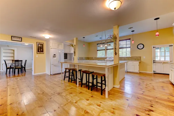 a large white kitchen with stainless steel appliances granite countertop a dining table chairs sink and cabinets