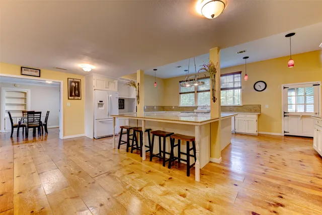 a large white kitchen with stainless steel appliances granite countertop a dining table chairs sink and cabinets