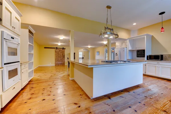 a large kitchen with kitchen island a island wooden floor stainless steel appliances and a chandelier