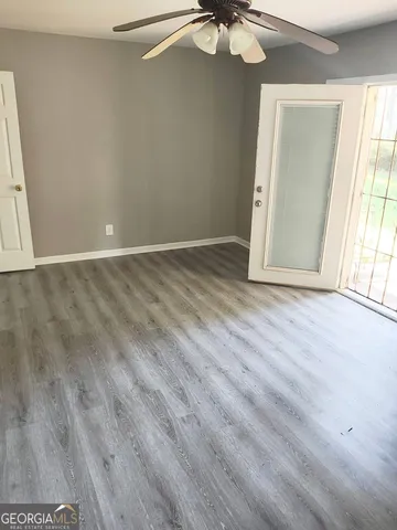 an empty room with wooden floor fan and windows