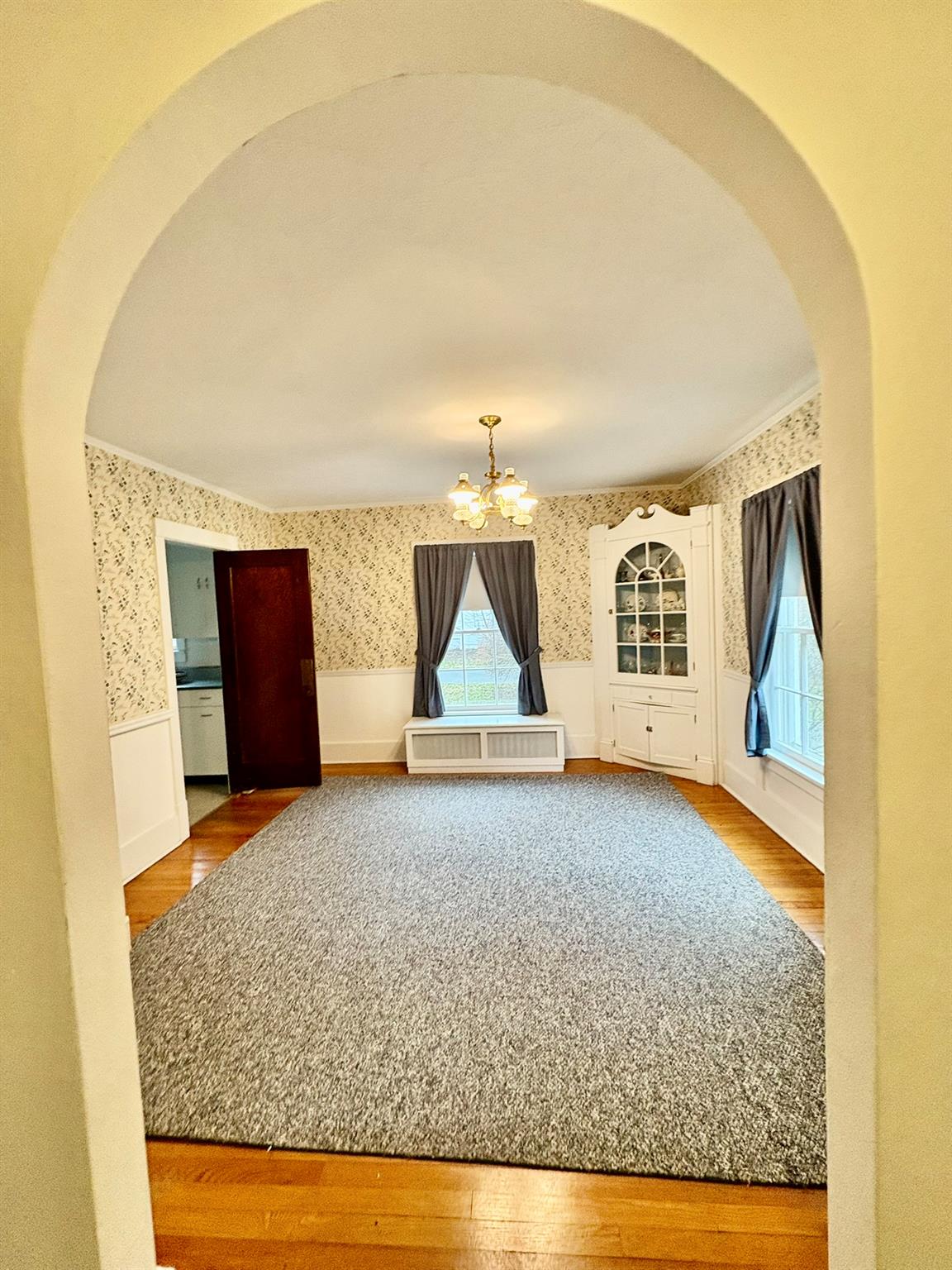 123 Rockland Road Roscoe, NY 12776 - Photo 11 of 31 View into DR from foyer featuring wood-type flooring, wainscoting, wallpapered walls, arched walkways, and an inviting chandelier