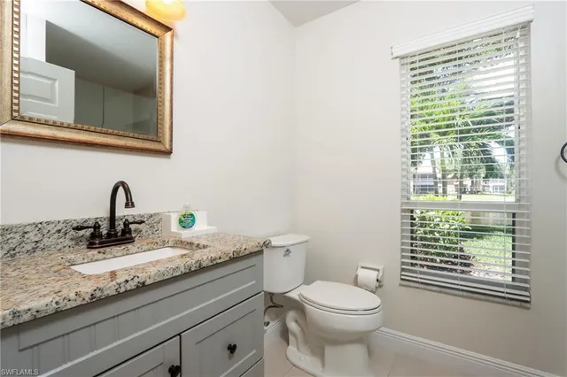 a bathroom with a granite countertop toilet a sink a mirror and a window