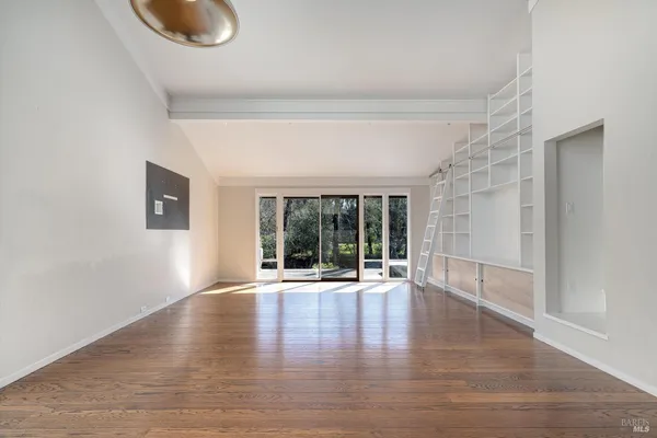 a view of empty room with wooden floor and kitchen