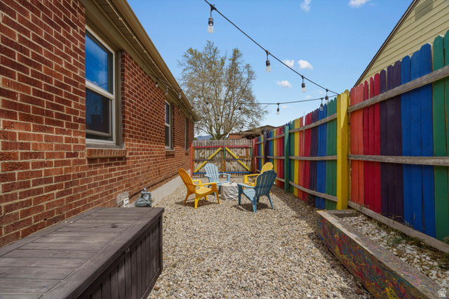 961 33rd Street Ogden, UT 84403 - Photo 30 of 39 Gravel-paved outdoor space featuring string lighting, a colorful privacy fence, and a brick exterior wall