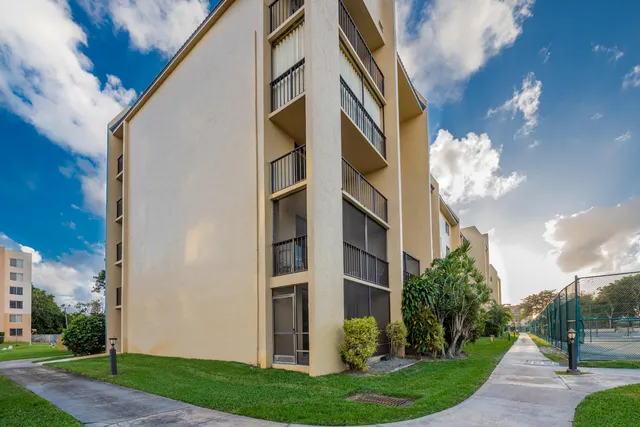 a view of a fountain in front of a big yard with plants and large trees