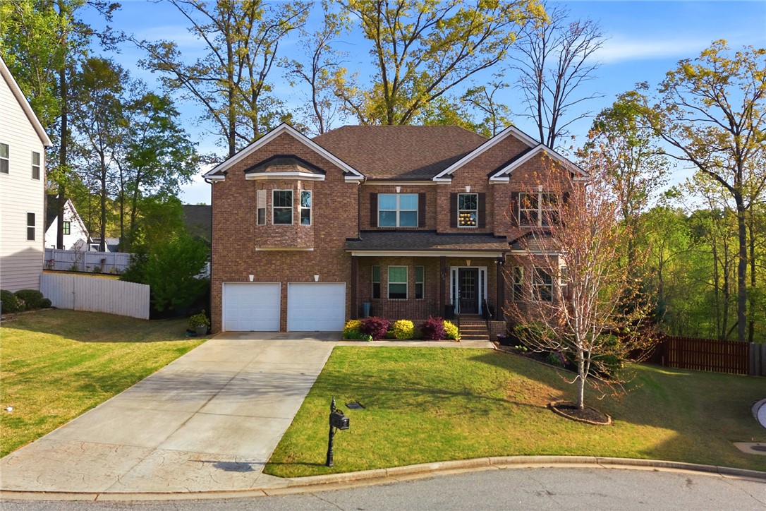 This classic brick residence features an attached garage and a welcoming front porch, nestled in a lush setting.