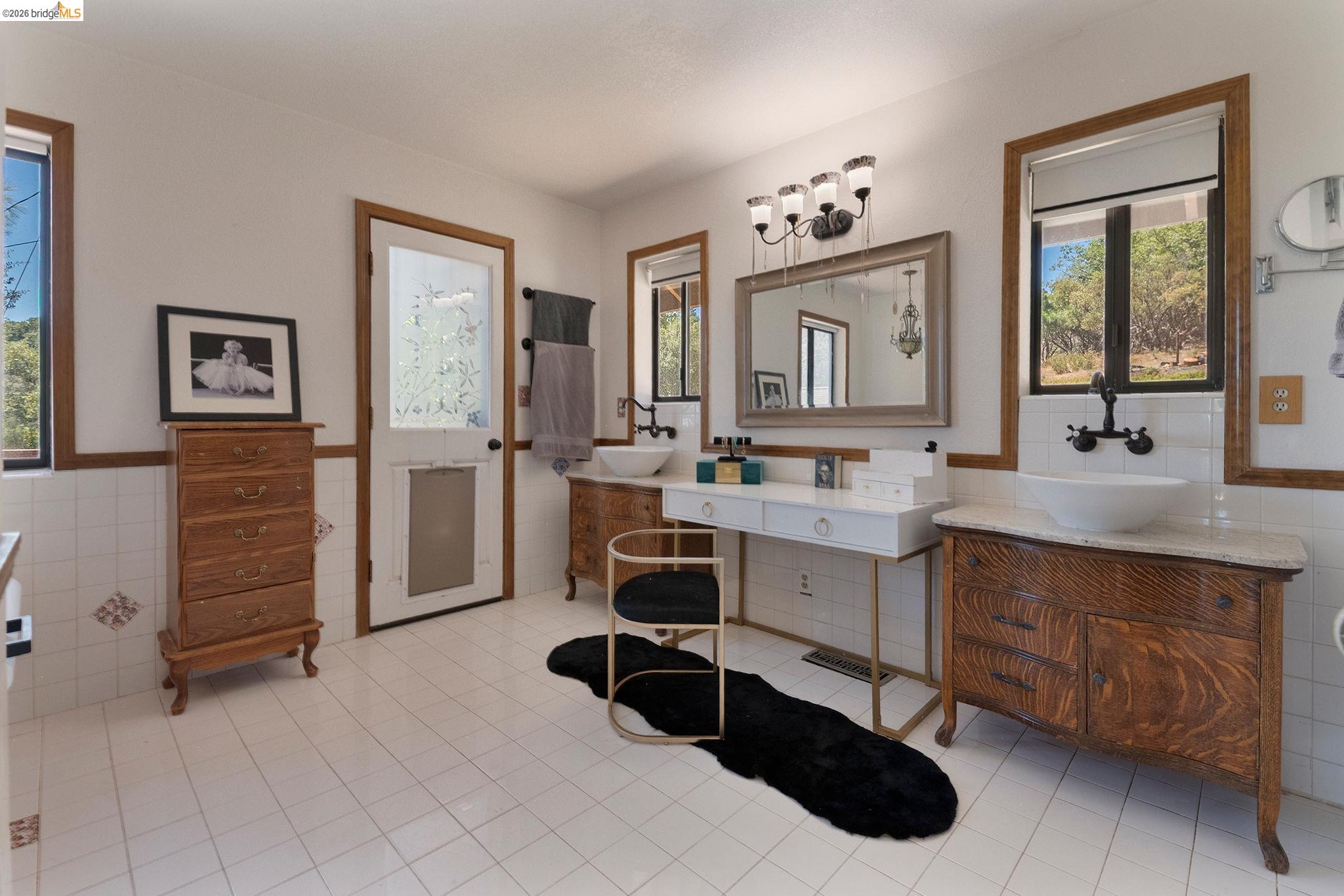22963 Robertson Ranch Road Sonora, CA 95370 - Photo 25 of 90 Bathroom featuring white tile flooring, dual wood-finish vanity cabinets with vessel sinks, a wall-mounted faucet, and a large mirror with integrated lighting