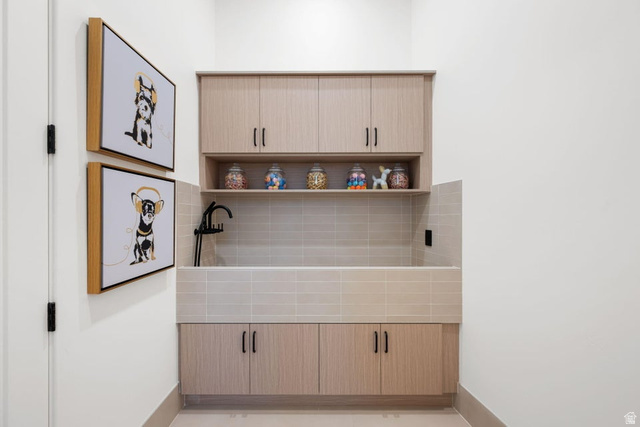 2867 East Granite Way St. George, UT 84790 - Photo 56 of 69 Dedicated utility space featuring a built-in wash basin with tiled surround, light wood-finish cabinetry, an open display shelf, and a matte black faucet