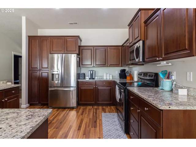 a kitchen with stainless steel appliances granite countertop a refrigerator a stove a sink and a wooden cabinets