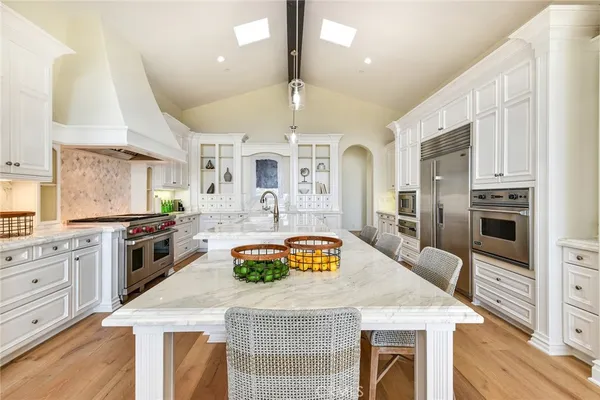 a kitchen with stainless steel appliances granite countertop a stove top oven a sink a refrigerator white cabinets and wooden floor