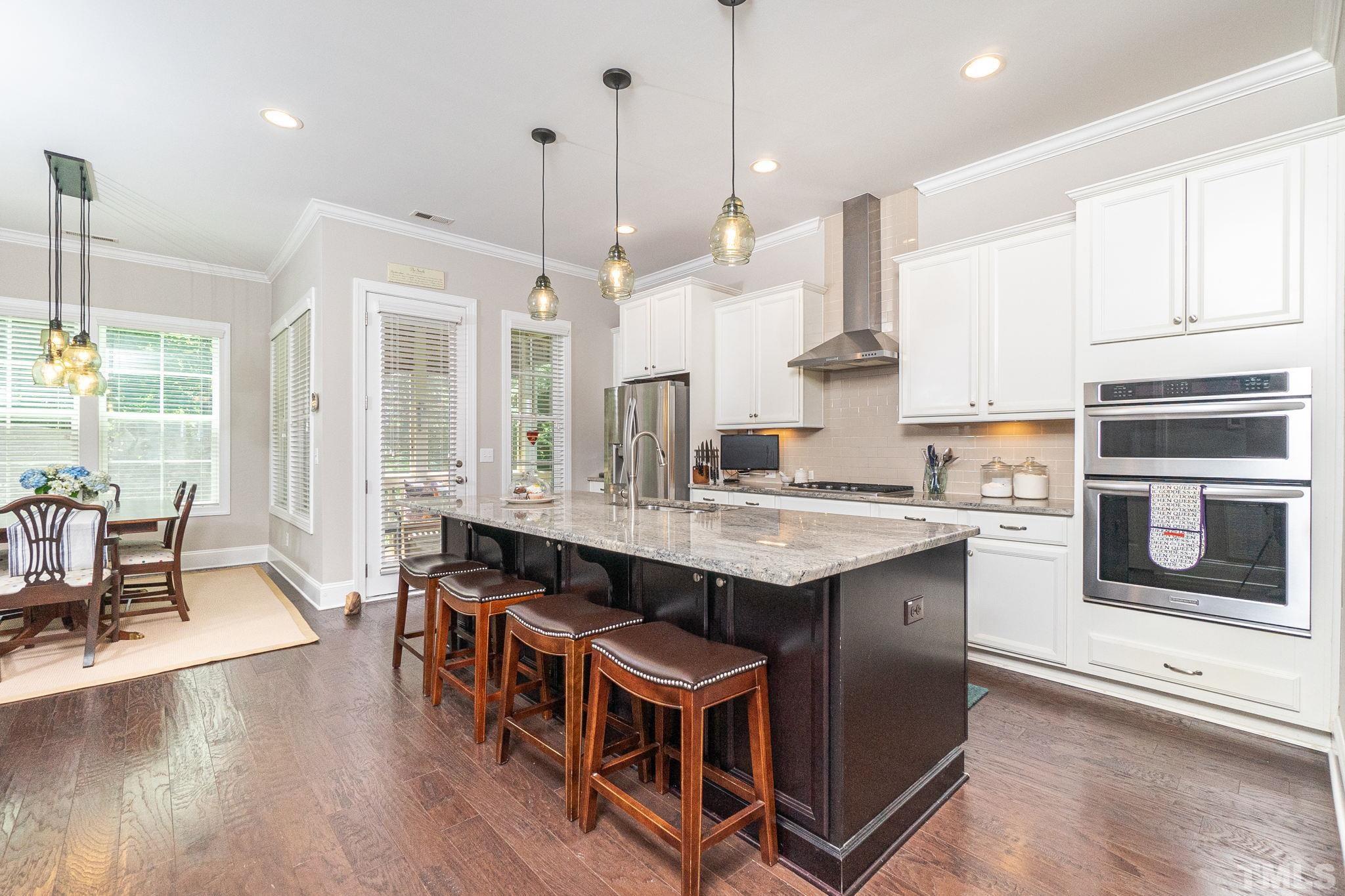 129 Penley Circle Raleigh, NC 27609 - Photo 14 of 43 a kitchen with stainless steel appliances granite countertop a stove a refrigerator a kitchen island a dining table and chairs with wooden floor