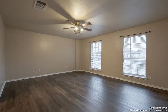 an empty room with wooden floor chandelier fan and windows