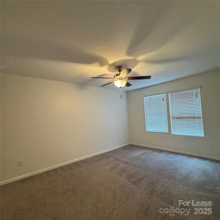 an empty room with a chandelier fan and windows