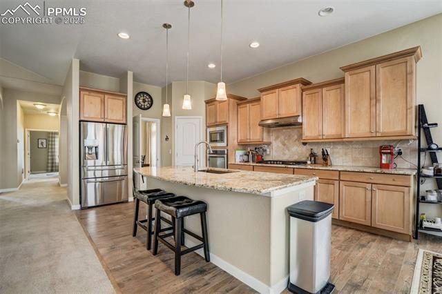 12442 Carmel Ridge Road Colorado Springs, CO 80921 - Photo 14 of 50 Kitchen with appliances with stainless steel finishes, pendant lighting, decorative backsplash, light stone countertops, and a center island with sink