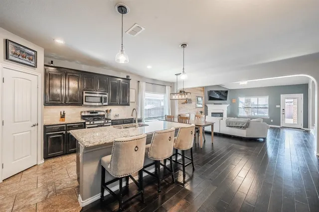 a kitchen with stainless steel appliances granite countertop a stove a refrigerator a kitchen island a dining table and chairs with wooden floor