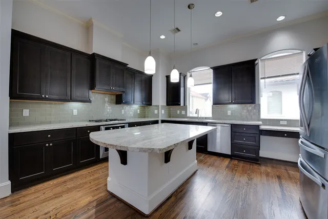 a kitchen with stainless steel appliances granite countertop wooden cabinets a sink a stove a refrigerator and island