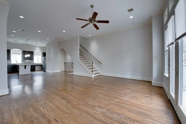 an empty room with wooden floor a ceiling fan and windows