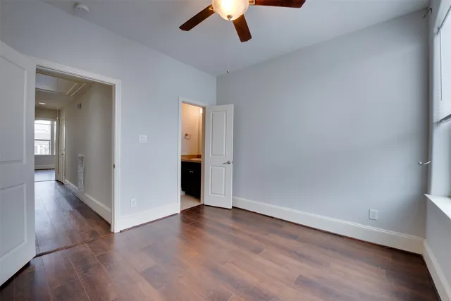 an empty room with wooden floor chandelier fan and windows