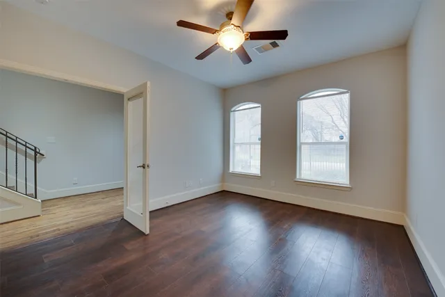 an empty room with wooden floor ceiling fan and windows