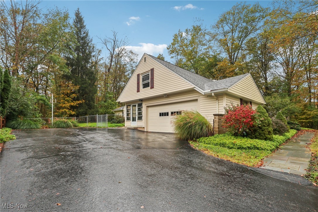 33300 South Woodland Road Cleveland, OH 44124 - Photo 4 of 50 View of home's exterior with asphalt driveway, a garage, roof with shingles, and view of wooded area