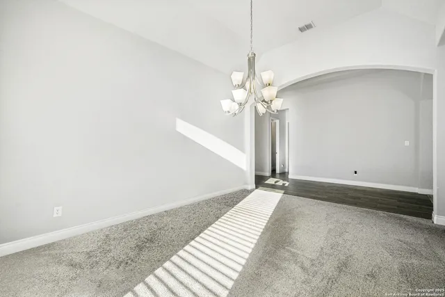a view of an empty room with chandelier fan and wooden floor