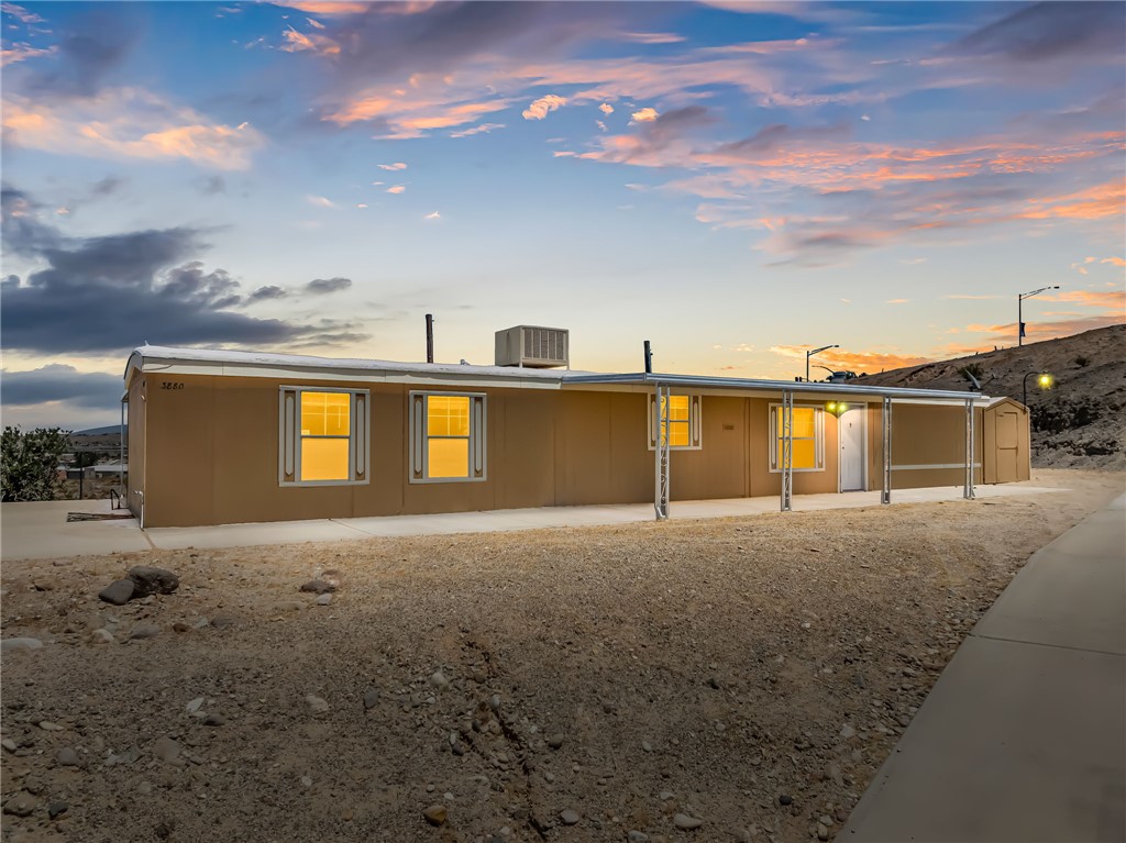 3880 Rising Sun Road Bullhead City, AZ 86442 - Photo 1 of 42 Tan single-story structure with multiple windows, an extended covered front patio, and an adjacent utility shed