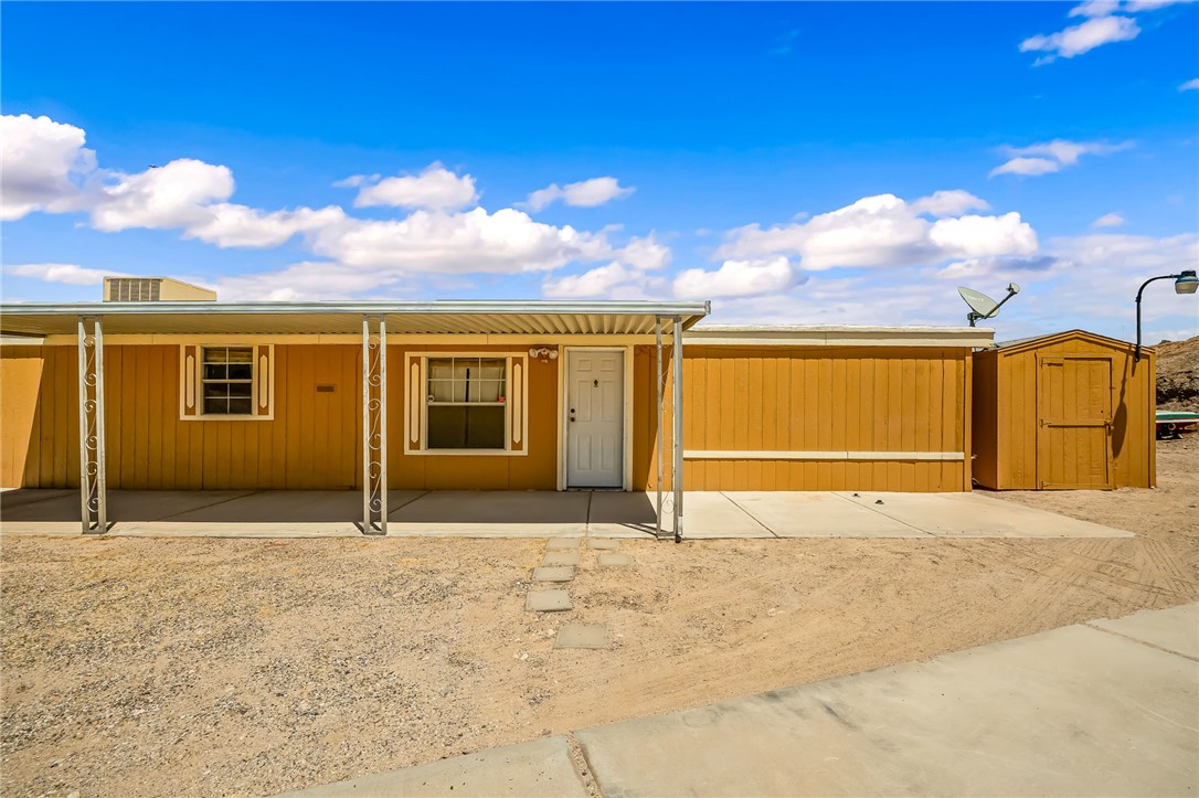3880 Rising Sun Road Bullhead City, AZ 86442 - Photo 3 of 42 Single-story residence featuring a covered front patio, two front-facing windows with decorative trim, a white entry door, and an exterior storage shed
