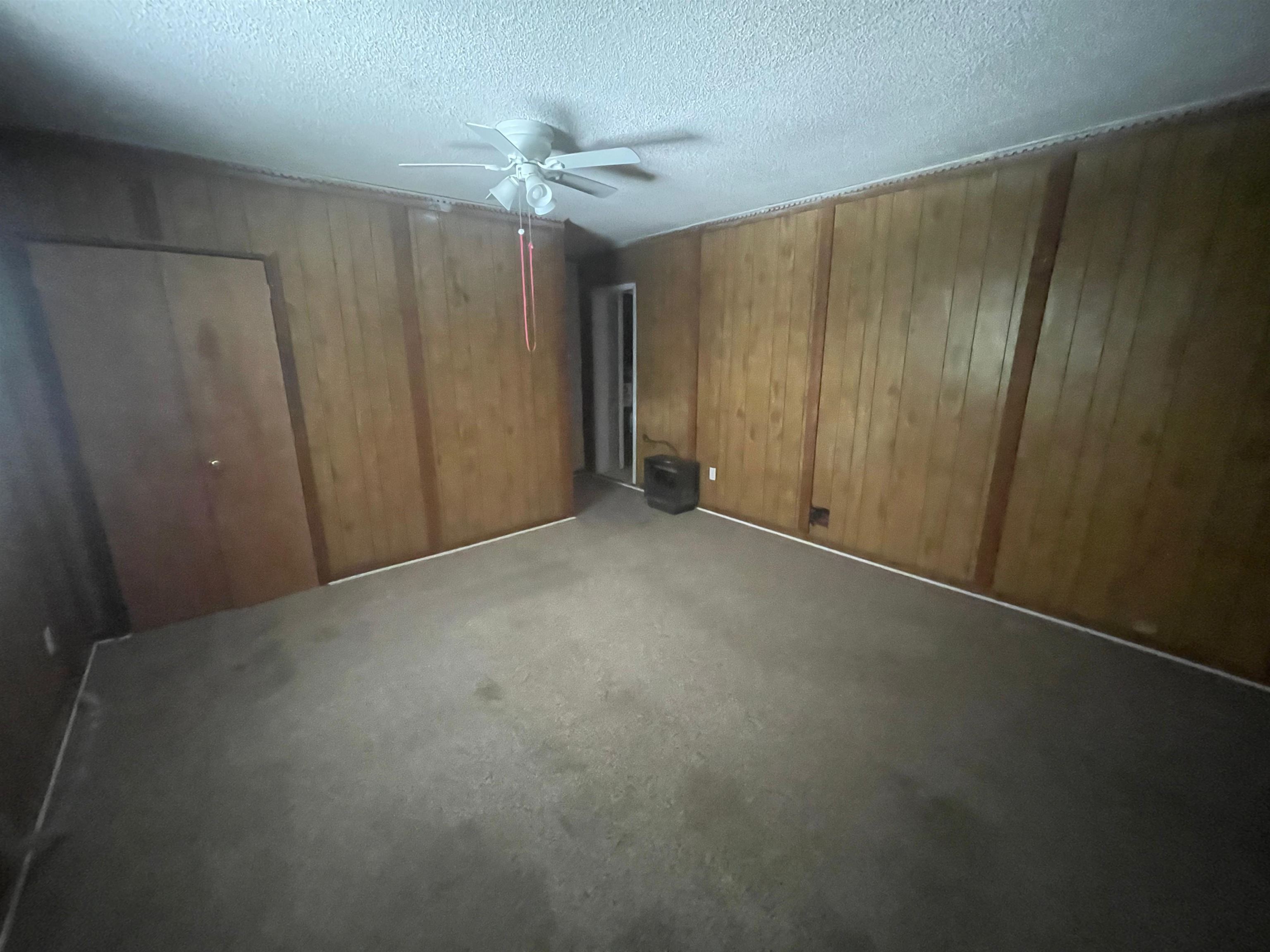 271 West Brooks Road Memphis, TN 38109 - Photo 13 of 17 Unfurnished bedroom with wooden walls, a textured ceiling, a closet, carpet flooring, and a ceiling fan