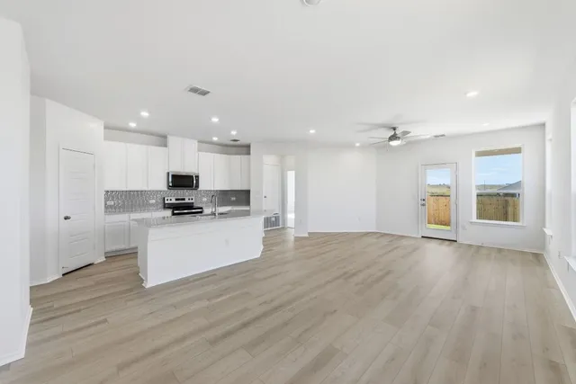 a view of kitchen with granite countertop refrigerator oven a sink and white cabinets with wooden floor