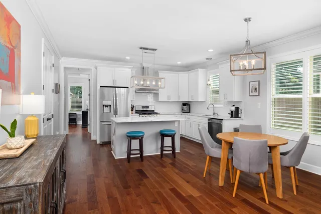 a kitchen with stainless steel appliances granite countertop a stove a refrigerator a kitchen island a dining table and chairs with wooden floor