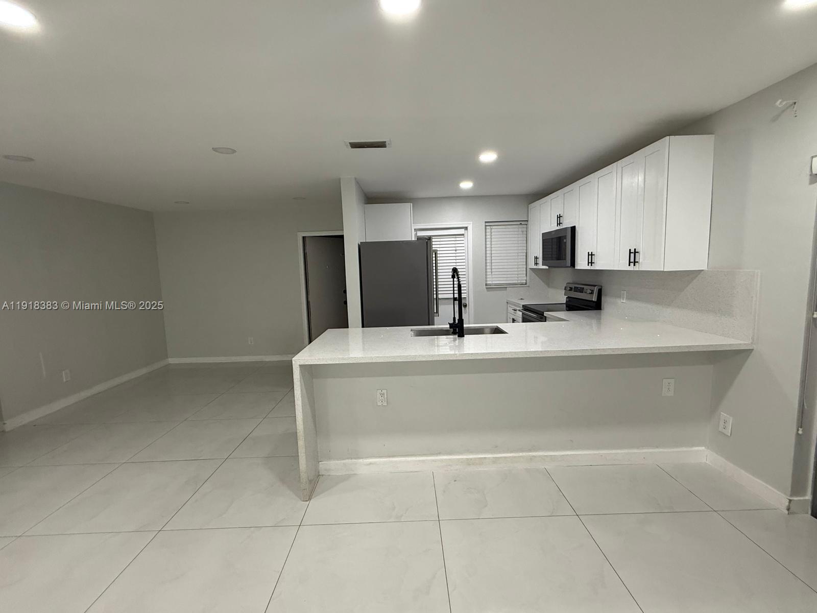 2461 Southwest 82nd Avenue, Unit 105 Davie, FL 33324 - Photo 12 of 17 a kitchen with kitchen island granite countertop a stove a sink a refrigerator white cabinets and a granite counter top