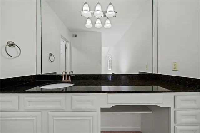 a bathroom with a granite countertop white cabinets and a sink