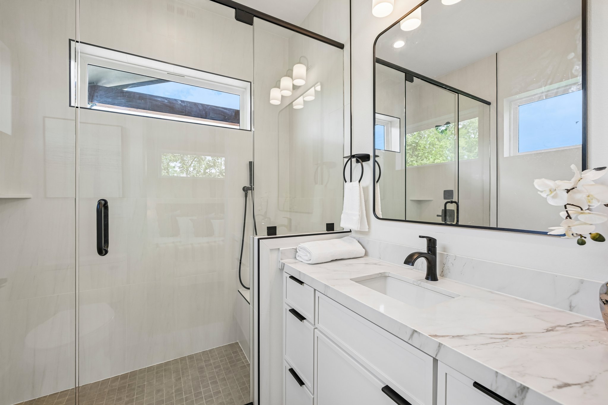 513 West Odell Street, Unit B Austin, TX 78752 - Photo 18 of 38 A contemporary bathroom with a bench, shower wand, and a spacious glass-enclosed shower alongside a vanity with plenty of drawers for storage.