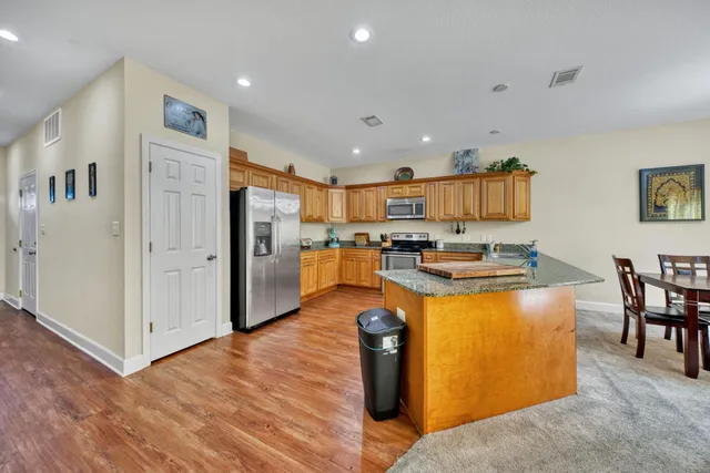 a open kitchen with stainless steel appliances granite countertop a stove top oven a refrigerator a dining table and chairs with wooden floor