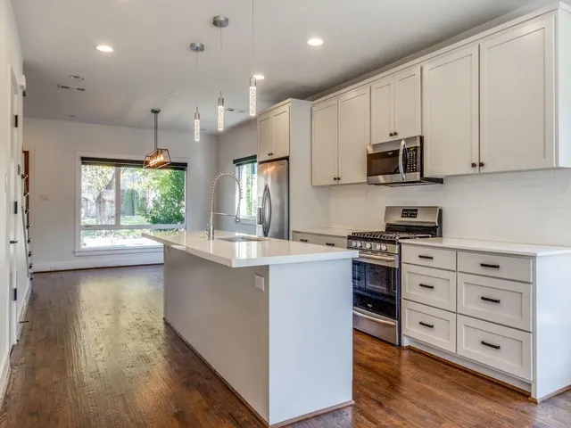 a kitchen with stainless steel appliances granite countertop a stove a sink and white cabinets with wooden floor