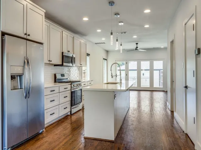 a kitchen with stainless steel appliances granite countertop a refrigerator a sink dishwasher a stove and white countertops with wooden floor