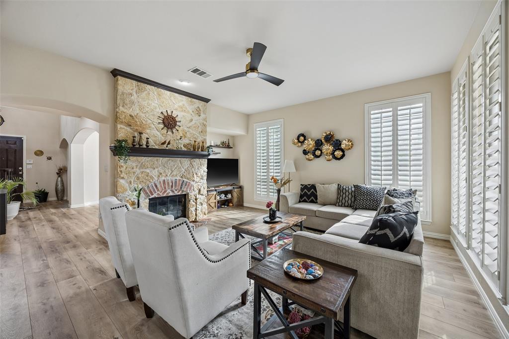 2865 Ridge View Road Frisco, TX 75034 - Photo 13 of 38 Stone-clad fireplace with a brick arch and dark wood mantel, wood-finish flooring, white plantation shutters, and a ceiling fan with integrated lighting