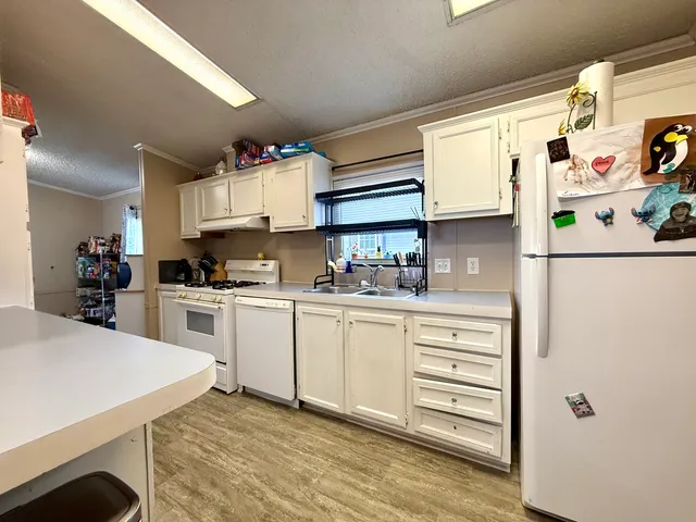 a kitchen with granite countertop a white refrigerator oven a sink dishwasher and white cabinets with wooden floor