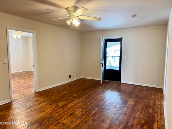 an empty room with wooden floor chandelier fan and windows