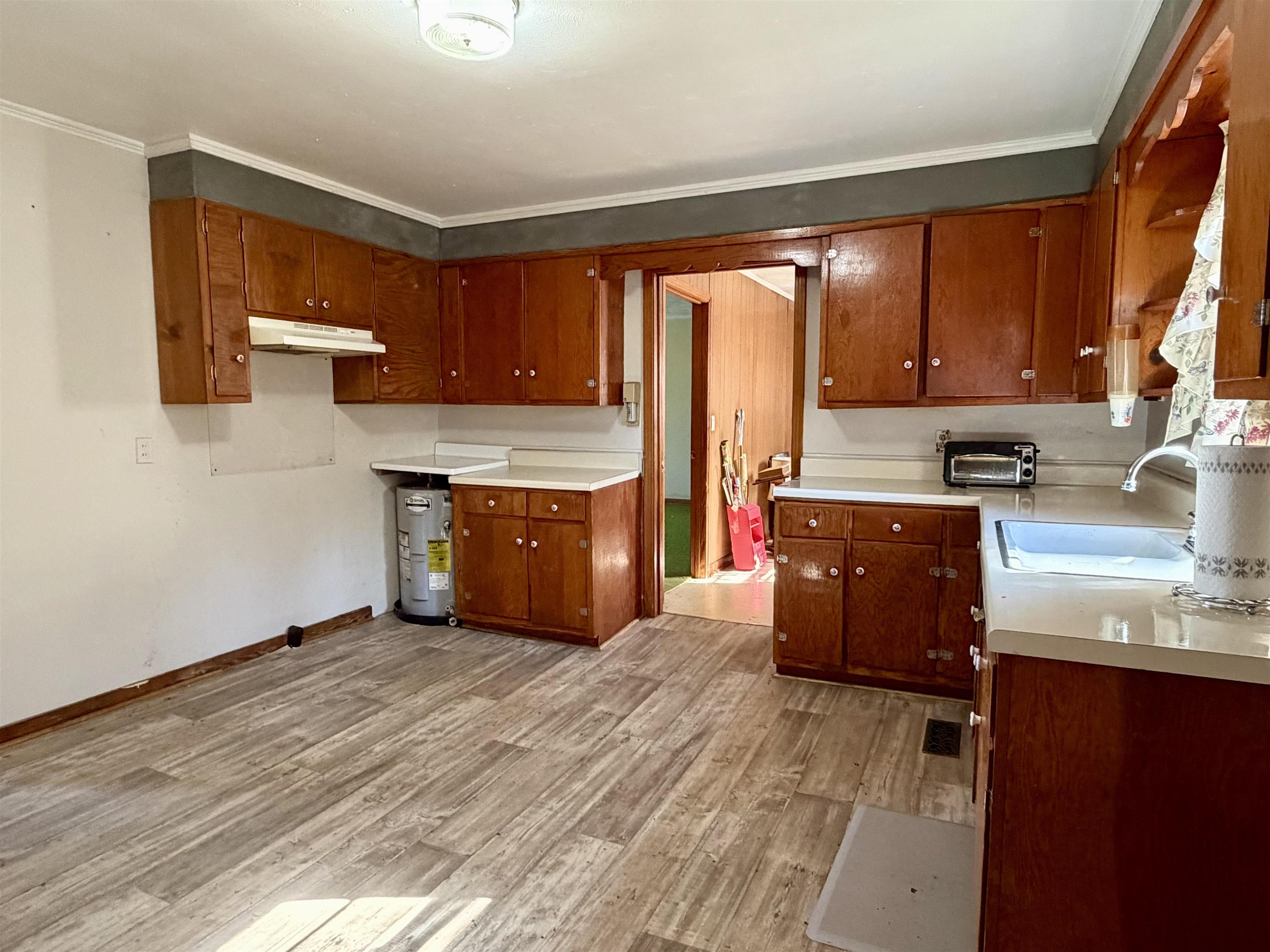 218 Sardie Henry Road Bethel Springs, TN 38315 - Photo 7 of 18 Kitchen featuring light countertops, wood finish cabinets, water heater, and ornamental molding