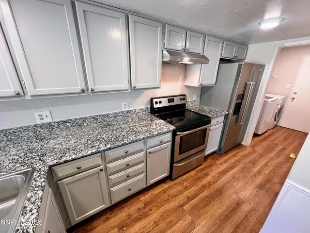 a kitchen with granite countertop a refrigerator a sink and white cabinets