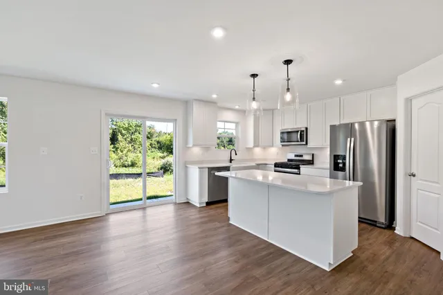 a kitchen with stainless steel appliances granite countertop a refrigerator a sink dishwasher a oven and a dining table with wooden floor