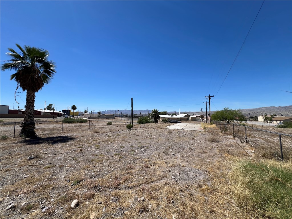 1692 Shamrock Road Bullhead City, AZ 86442 - Photo 11 of 11 The property features a large, undeveloped lot with a chain-link fence, a palm tree, and clear views of the surrounding landscape and distant hills