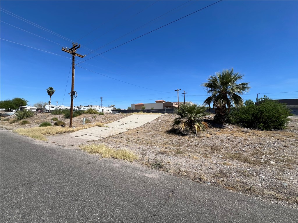 1692 Shamrock Road Bullhead City, AZ 86442 - Photo 2 of 11 The property features a paved road frontage, a utility pole with overhead lines, and established palm trees and shrubs
