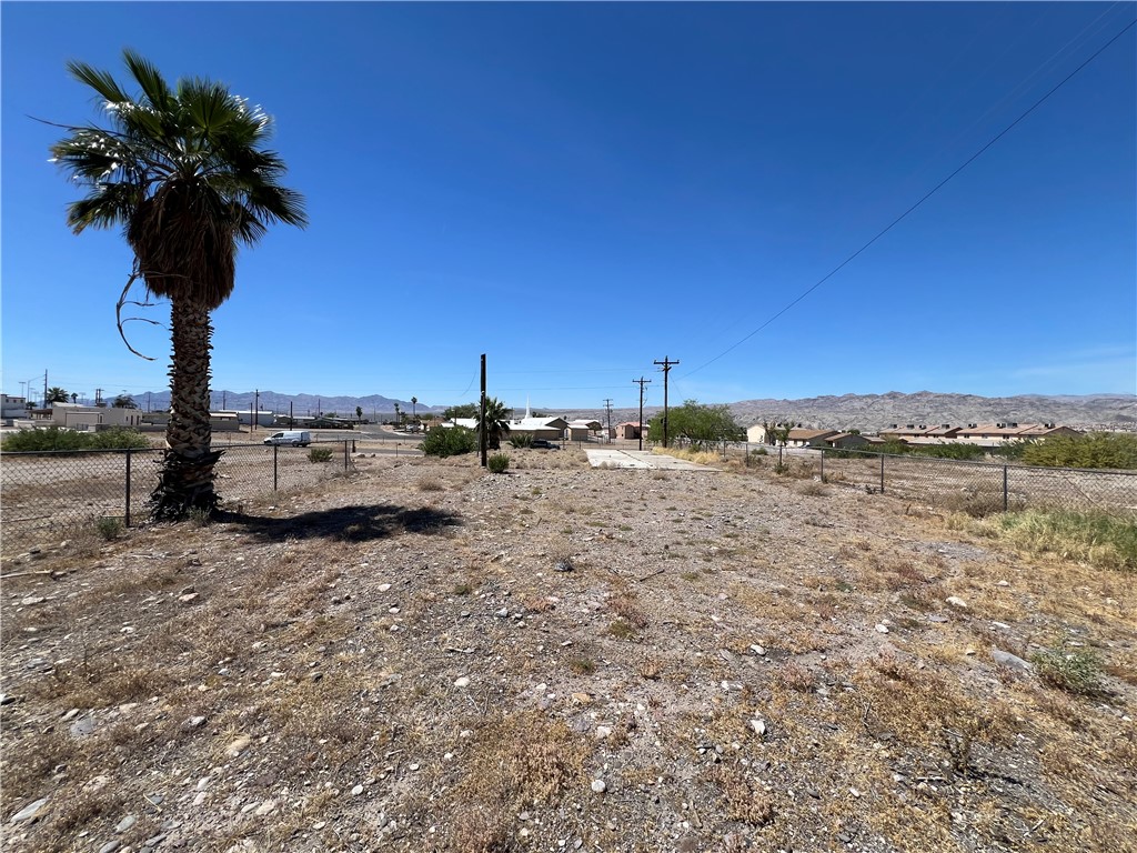1692 Shamrock Road Bullhead City, AZ 86442 - Photo 10 of 11 The property features an expansive lot with a palm tree, chain link fencing, and distant mountain views