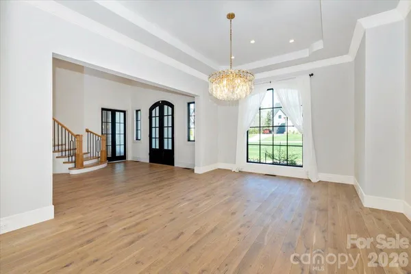 a view of an empty room with wooden floor kitchen view and a window